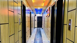 Un couloir aux murs lambrés et au sol en marbre, qui mène à une porte noire au fond.