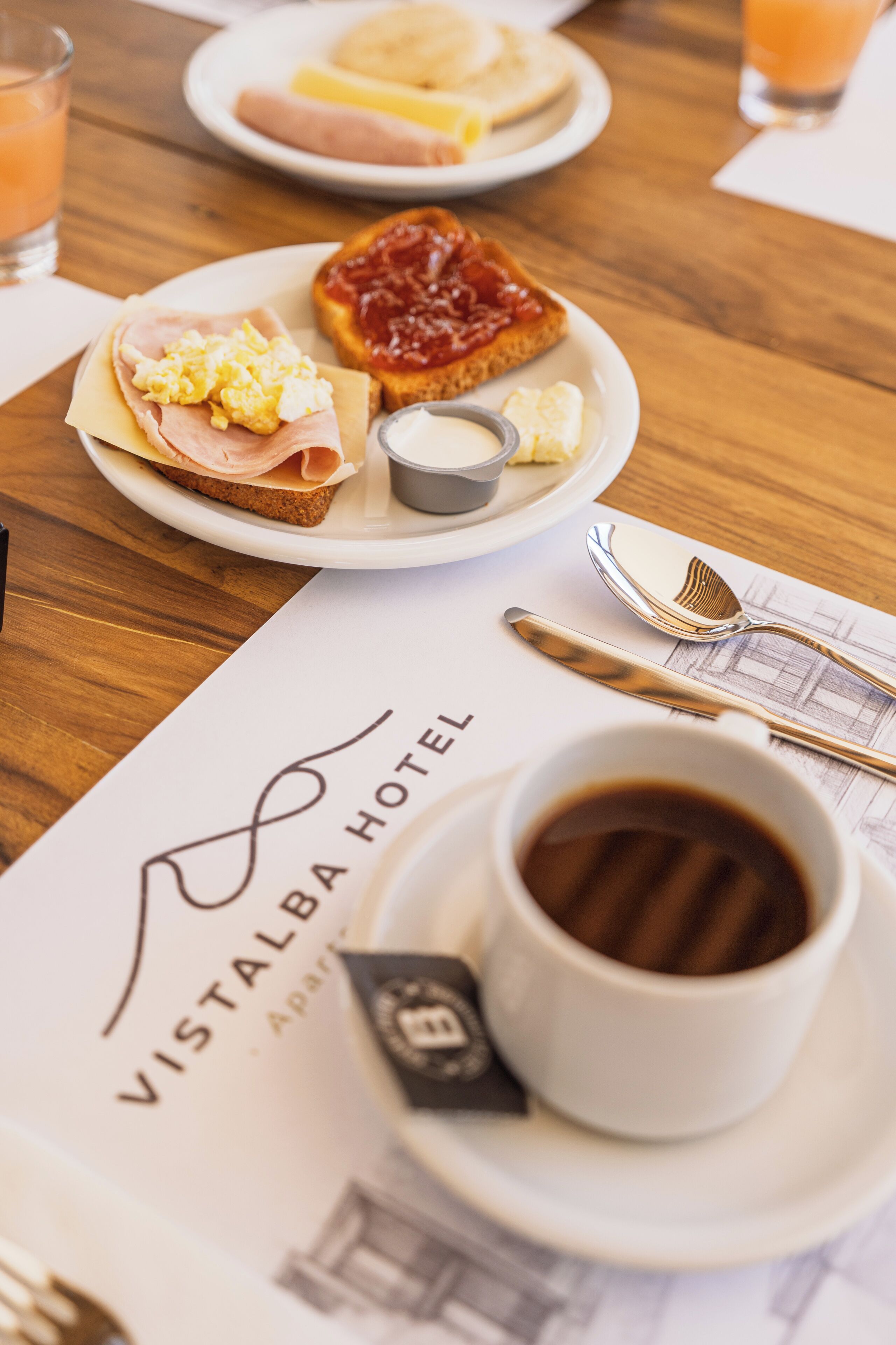 Desayuno con tostadas, huevos revueltos, jamón y una taza de café sobre una mesa con un menú del Hotel VistaBa.