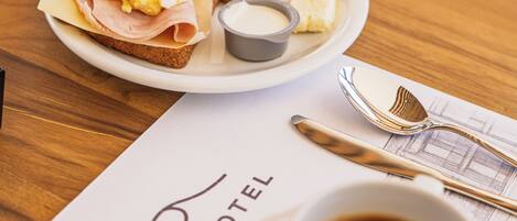 A breakfast setting with toast, scrambled eggs, ham, and a cup of coffee on a table with a menu from VistaBa Hotel.