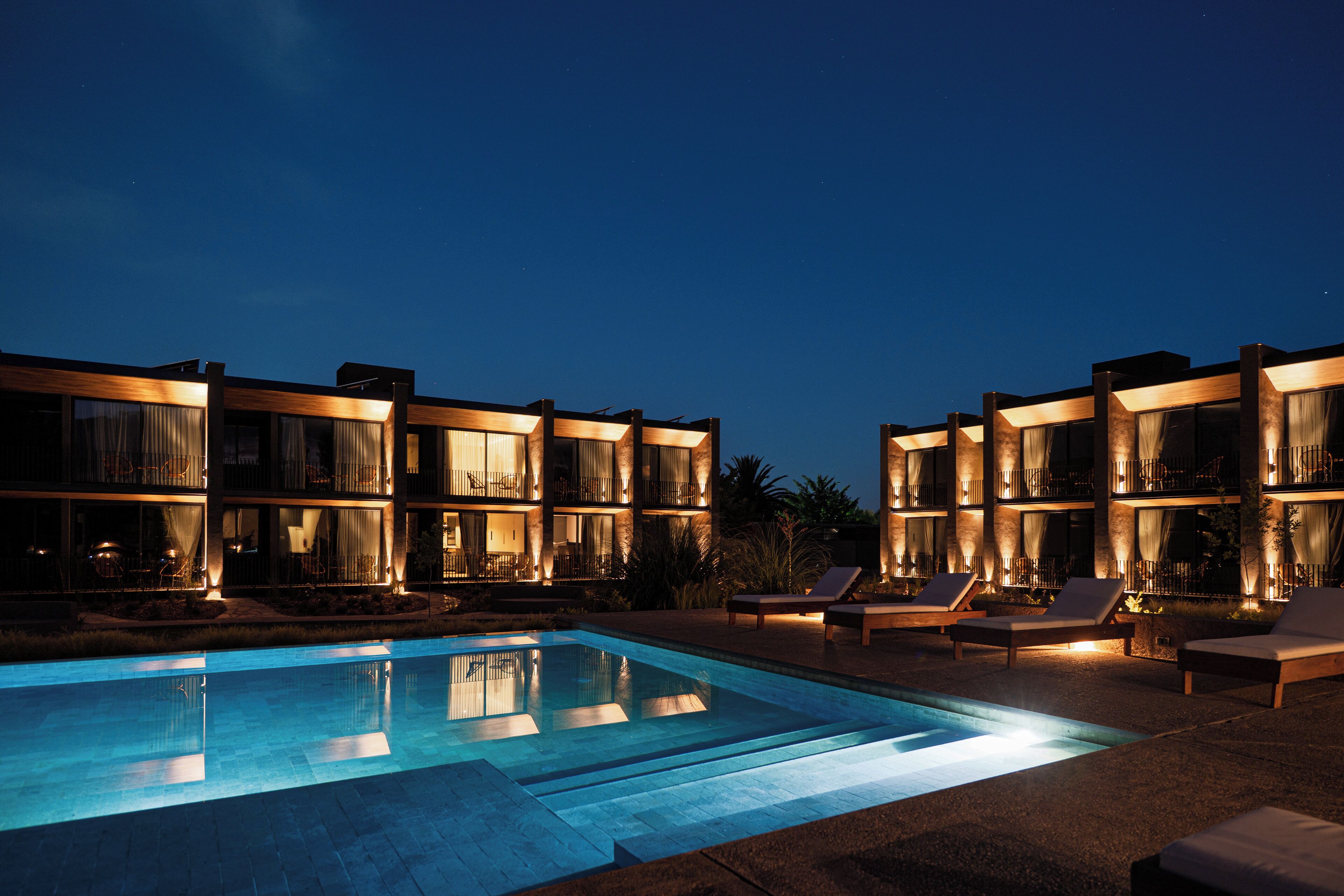 Um hotel moderno com piscina, espreguiçadeiras e fachada bem iluminada à noite.