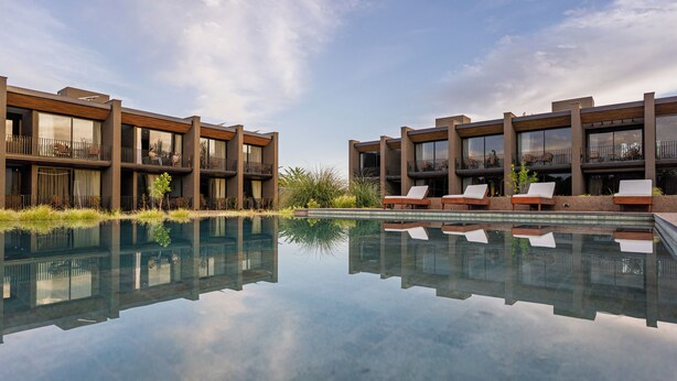 A modern hotel with a reflective pool, outdoor seating, and large windows. - Vistalba Hotel  Aparts & Suites (Luján de Cuyo)