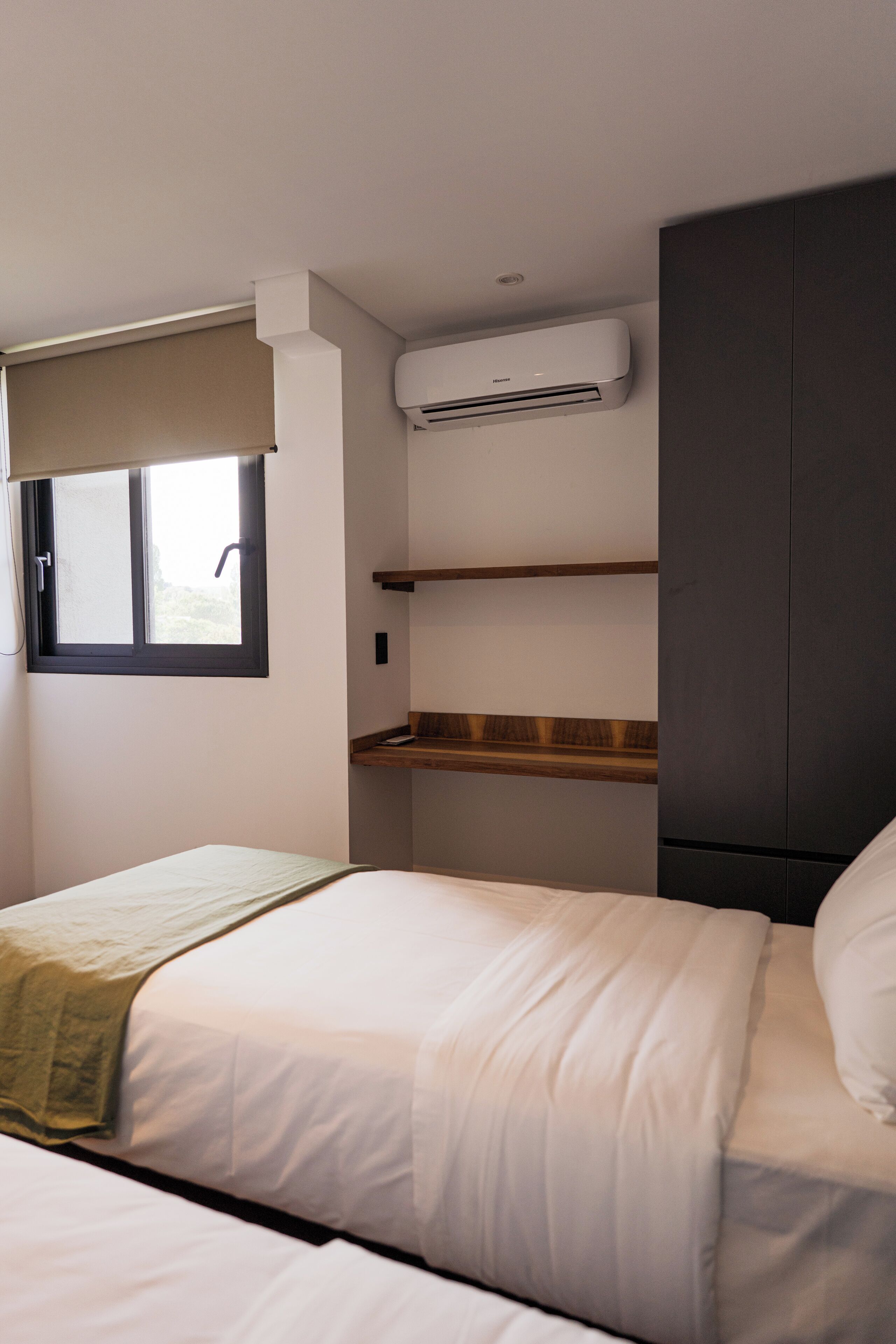 Une chambre à coucher comprenant un lit, une fenêtre avec un store, une étagère intégrée et une armoire.