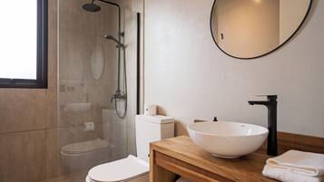 Une salle de bain moderne avec une douche à parois de verre, des toilettes blanches, un meuble-lavabo en bois avec un grand lavabo blanc et un miroir rond.