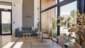A modern interior with a sofa, chairs, a coffee table, and large windows offering a view of greenery. - Vistalba Hotel  Aparts & Suites (Luján de Cuyo)