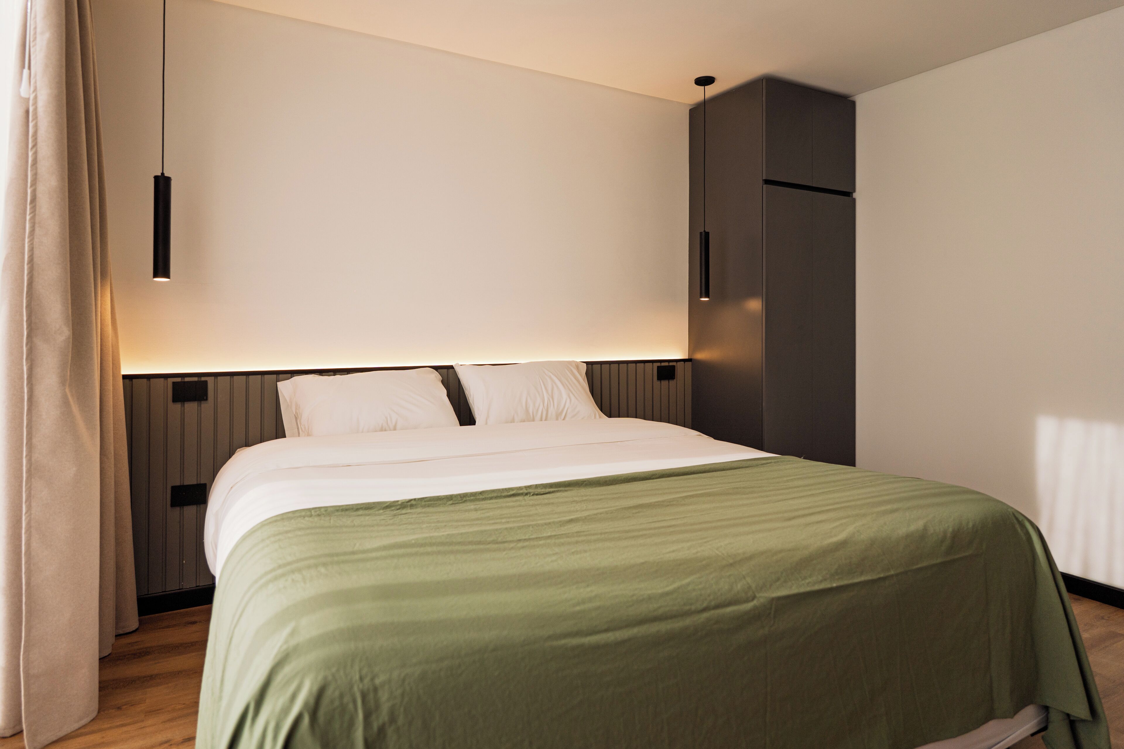 Una habitación de hotel moderna con una cama bien hecha, una mesita de noche y un armario.
