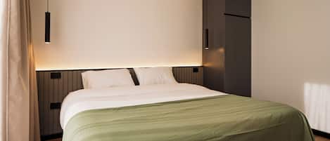 Una habitación de hotel moderna con una cama bien hecha, una mesita de noche y un armario.