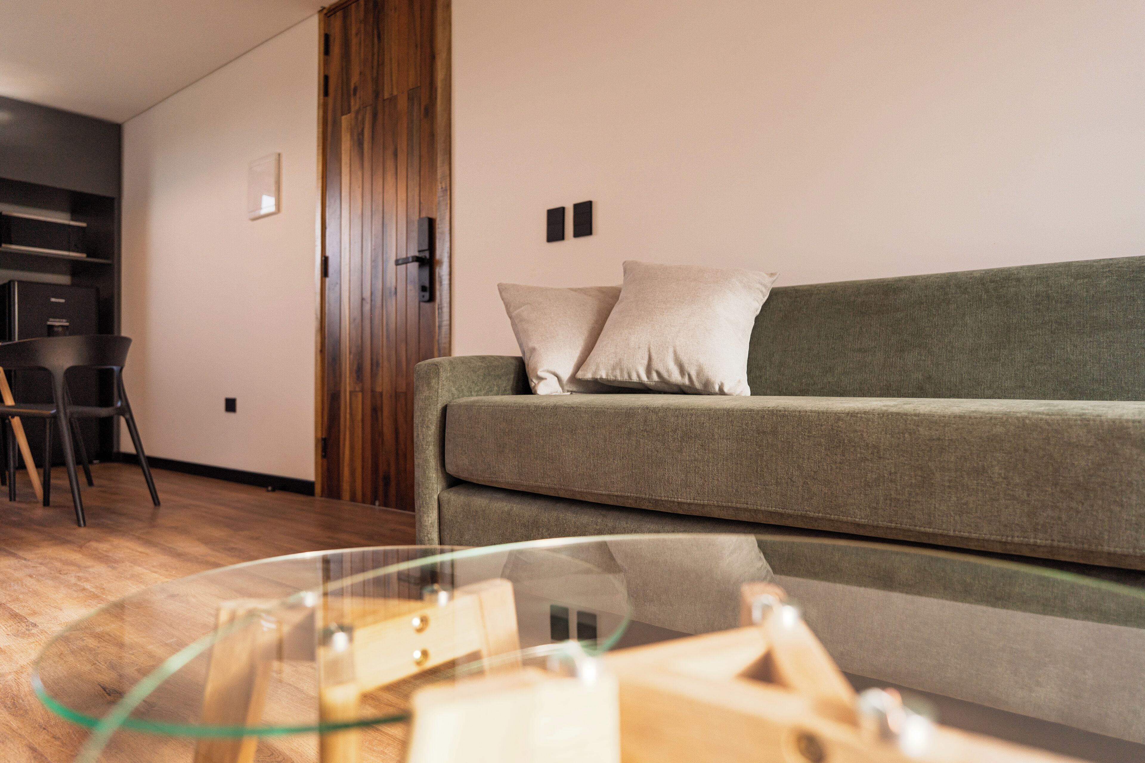 Ein modernes Wohnzimmer mit einem grünen Sofa, zwei Kissen, einem Glastisch und einer Holztür.