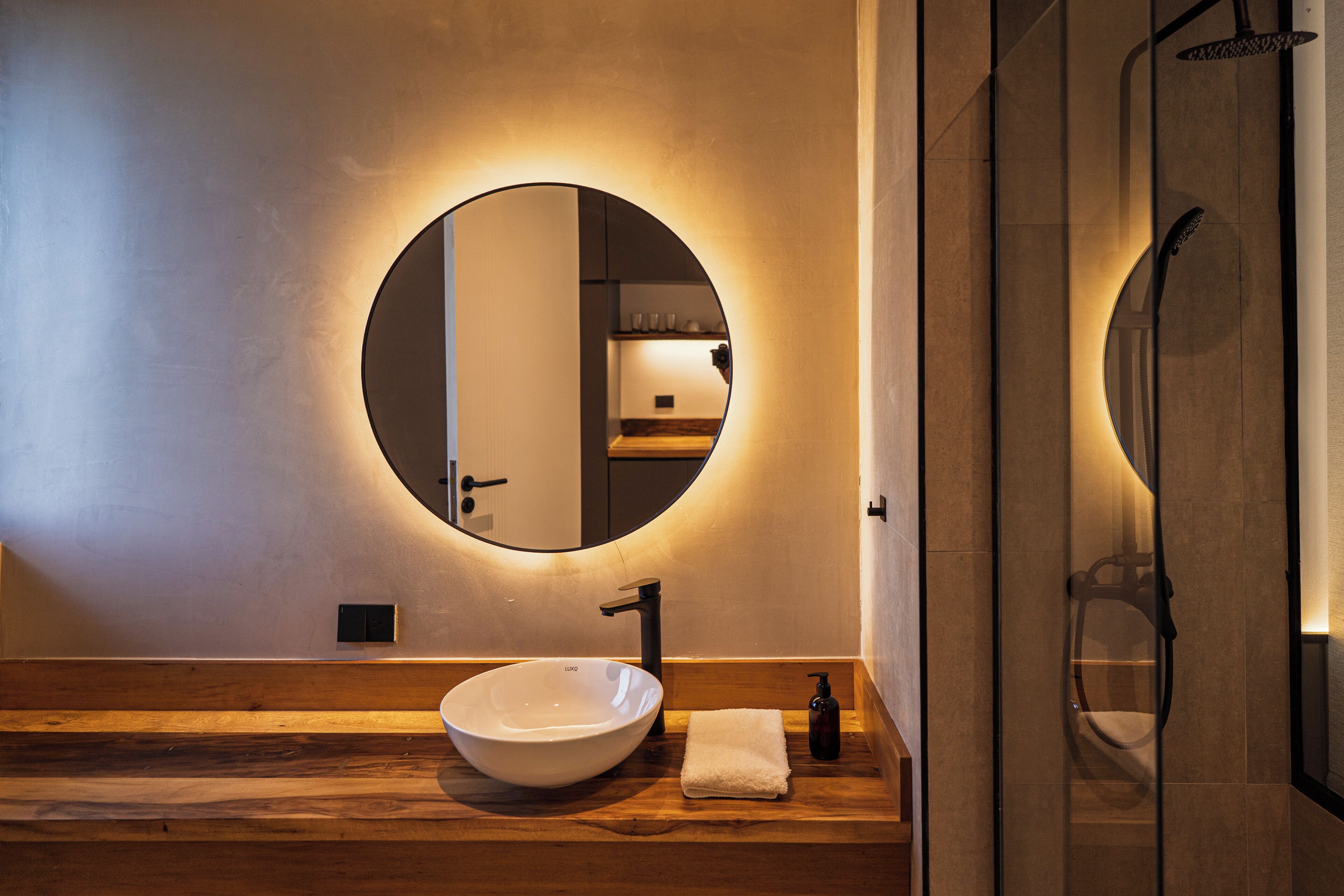 Un baño moderno con un espejo redondo, un lavabo sobre encimera y un mueble de tocador de madera.