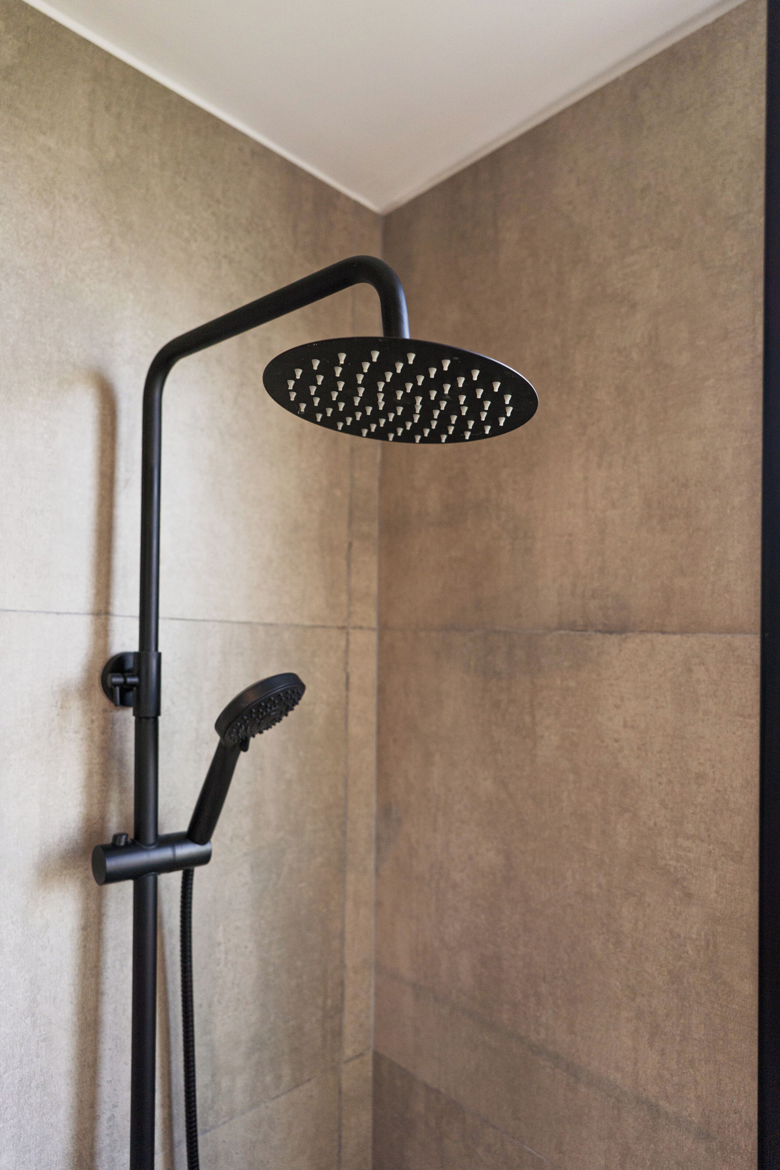 A shower with a handheld showerhead and a fixed overhead showerhead in a modern bathroom with tiled walls.