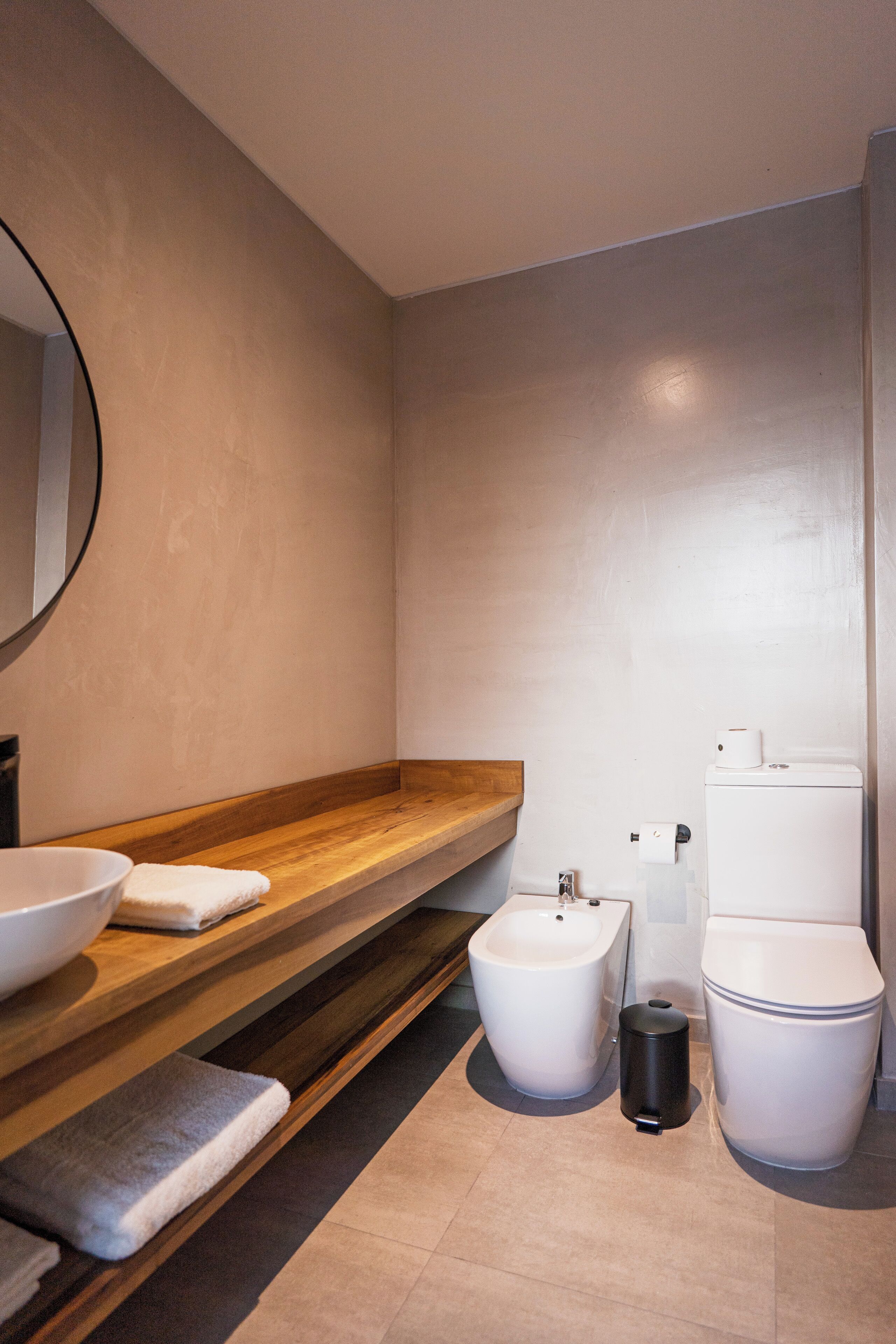 A modern bathroom with a wooden vanity, a bidet, a toilet, and a trash can.