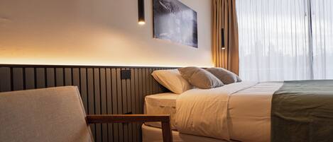A modern hotel room with a bed, a chair, a wall-mounted artwork, and a window with curtains.