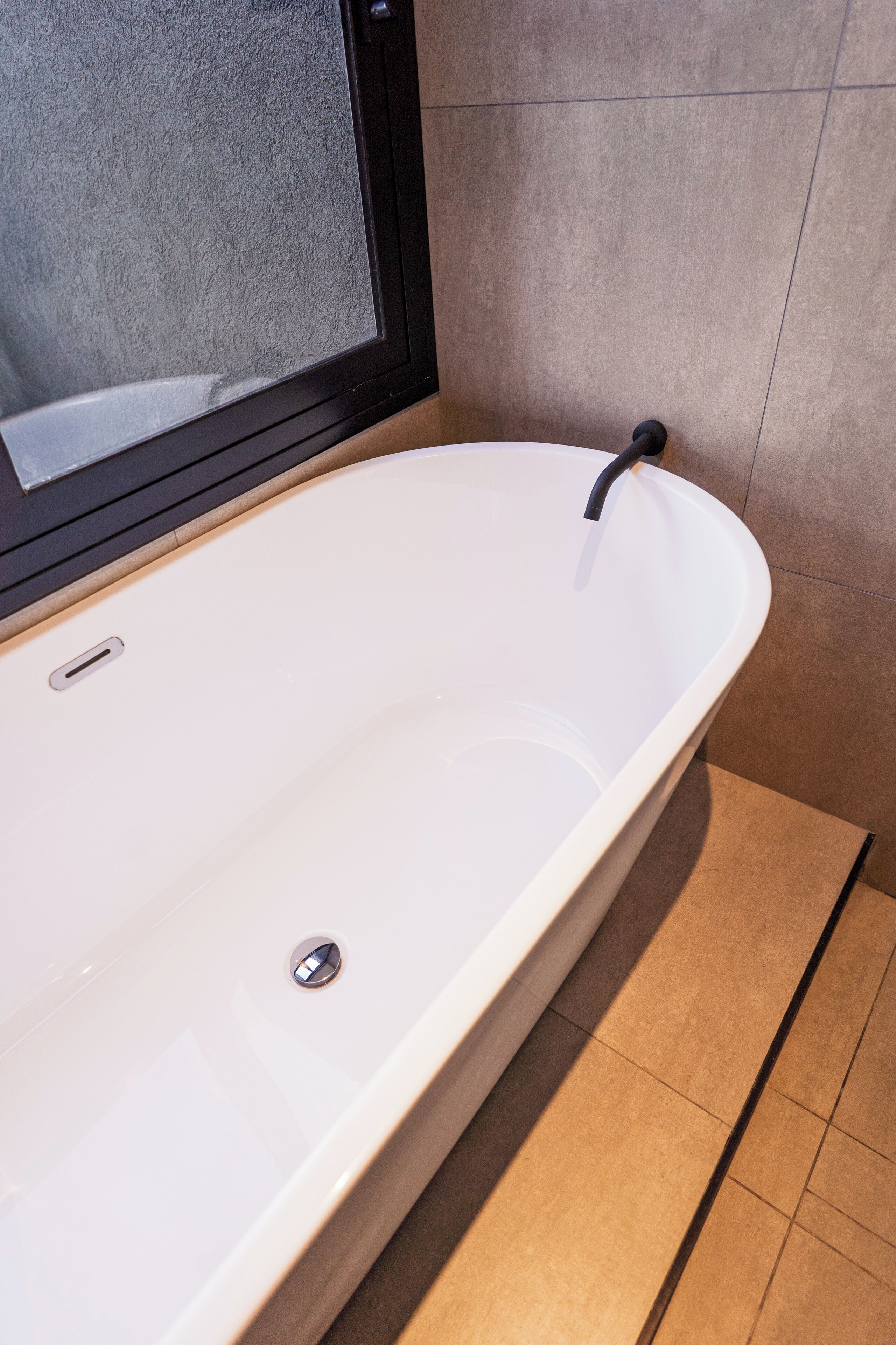A modern bathroom with a freestanding bathtub, a window, and tiled walls.