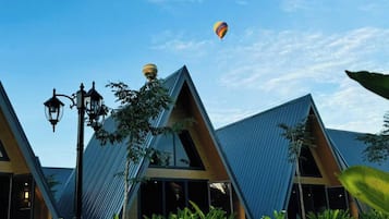 Una hilera de edificios modernos con techos triangulares, un cielo azul despejado y globos aerostáticos al fondo.