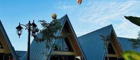 Una hilera de edificios modernos con techos triangulares, un cielo azul despejado y globos aerostáticos al fondo.