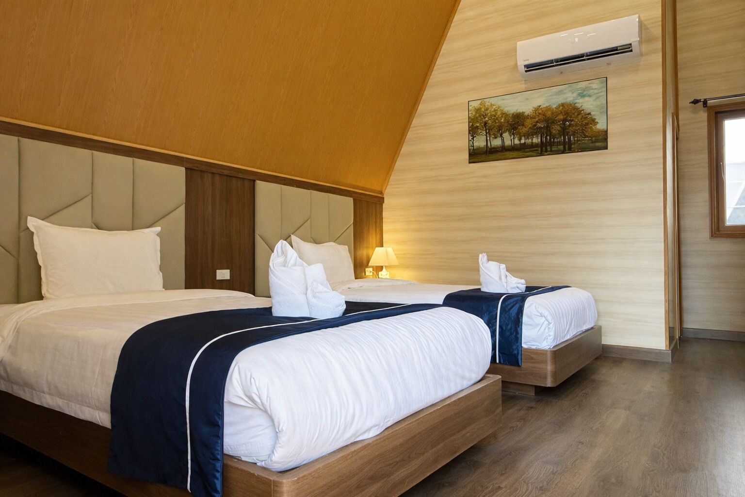 Et hotelværelse med to senge, en træsenggavl, et billede på væggen og en aircondition.