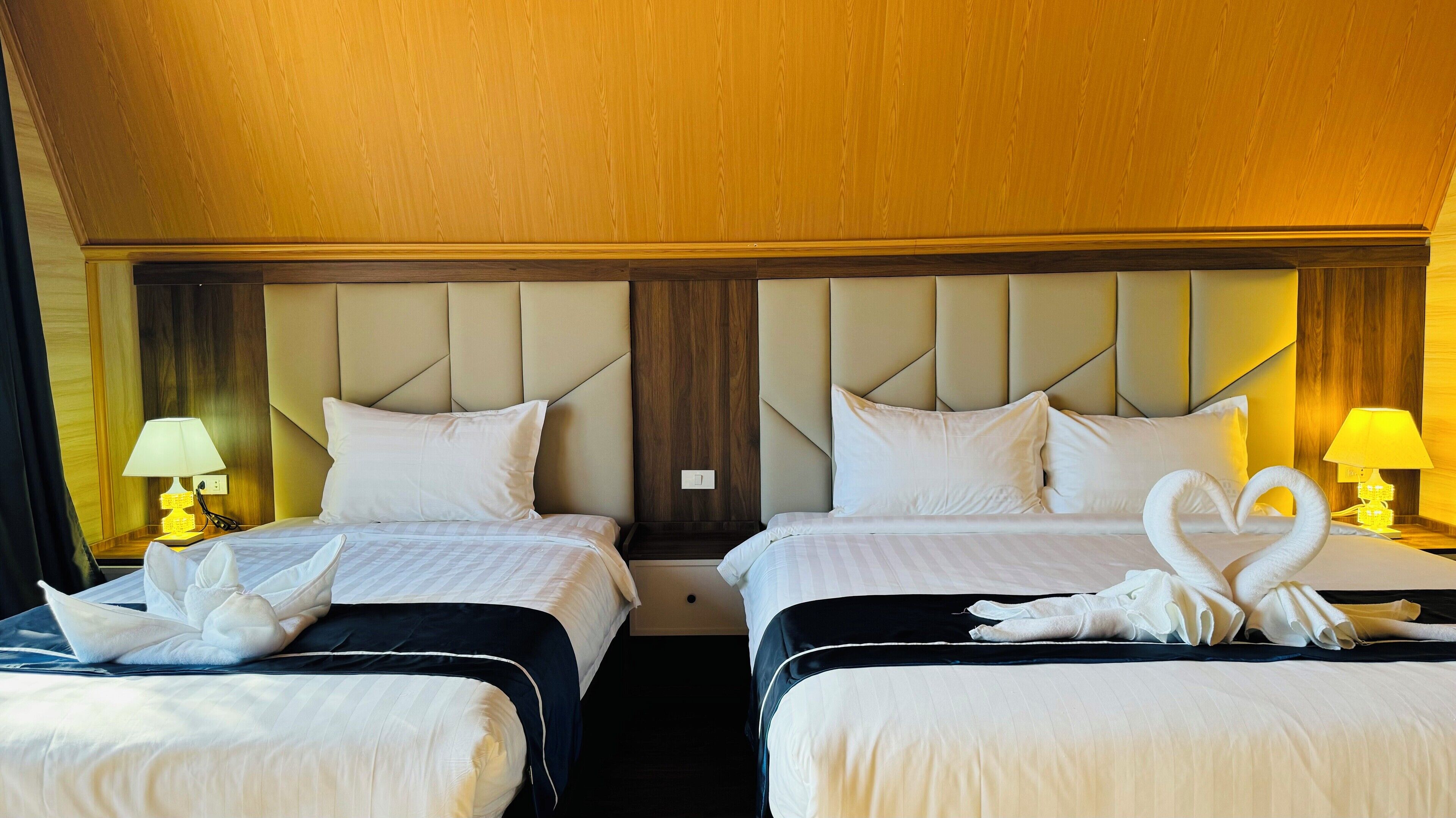 Habitación de hotel con dos camas, cada una con cabecera, ropa de cama blanca y un par de toallas blancas. Hay lámparas de noche a cada lado de las camas.