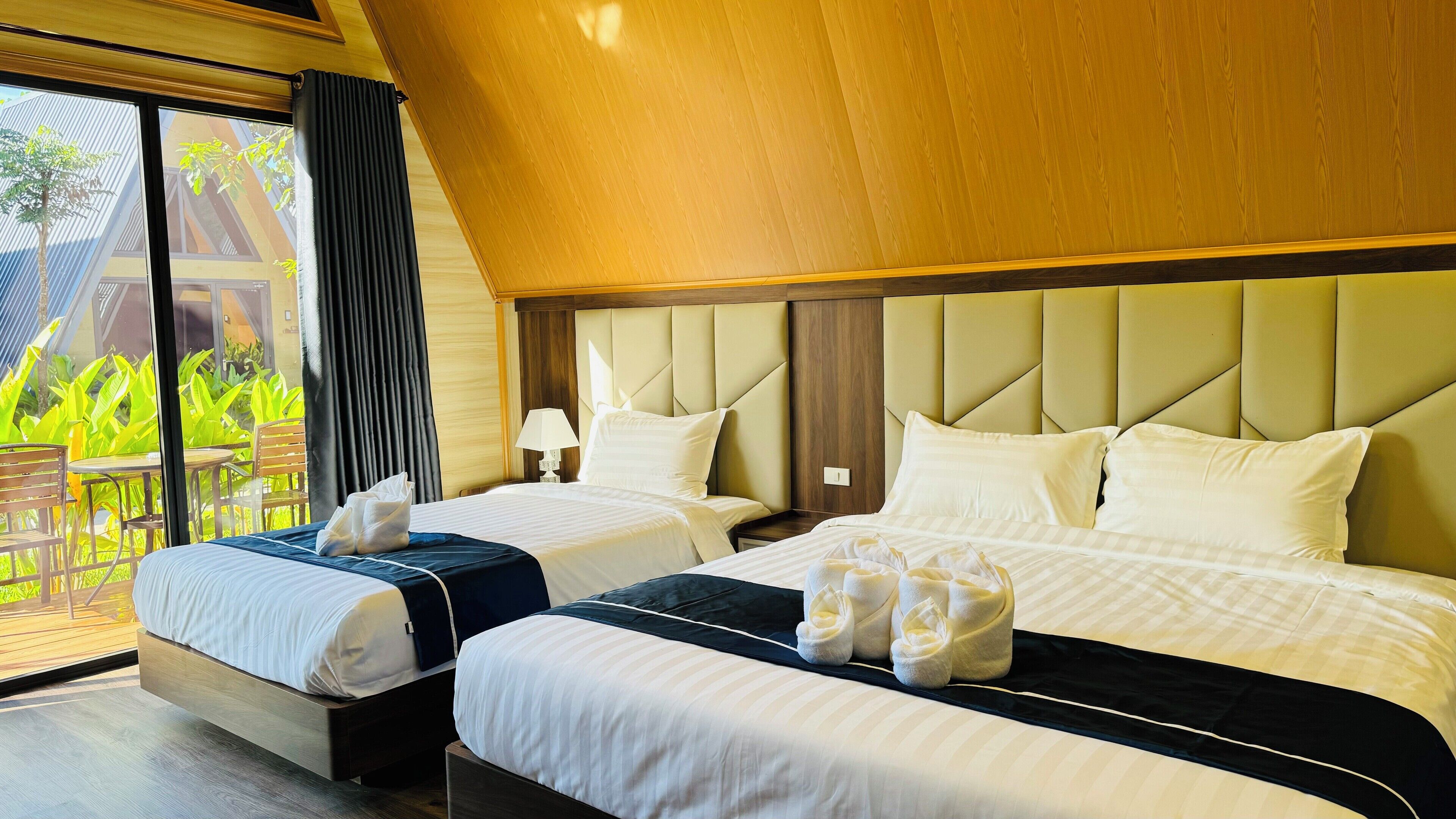 A hotel room with two beds, a wooden ceiling, and a view of greenery outside.