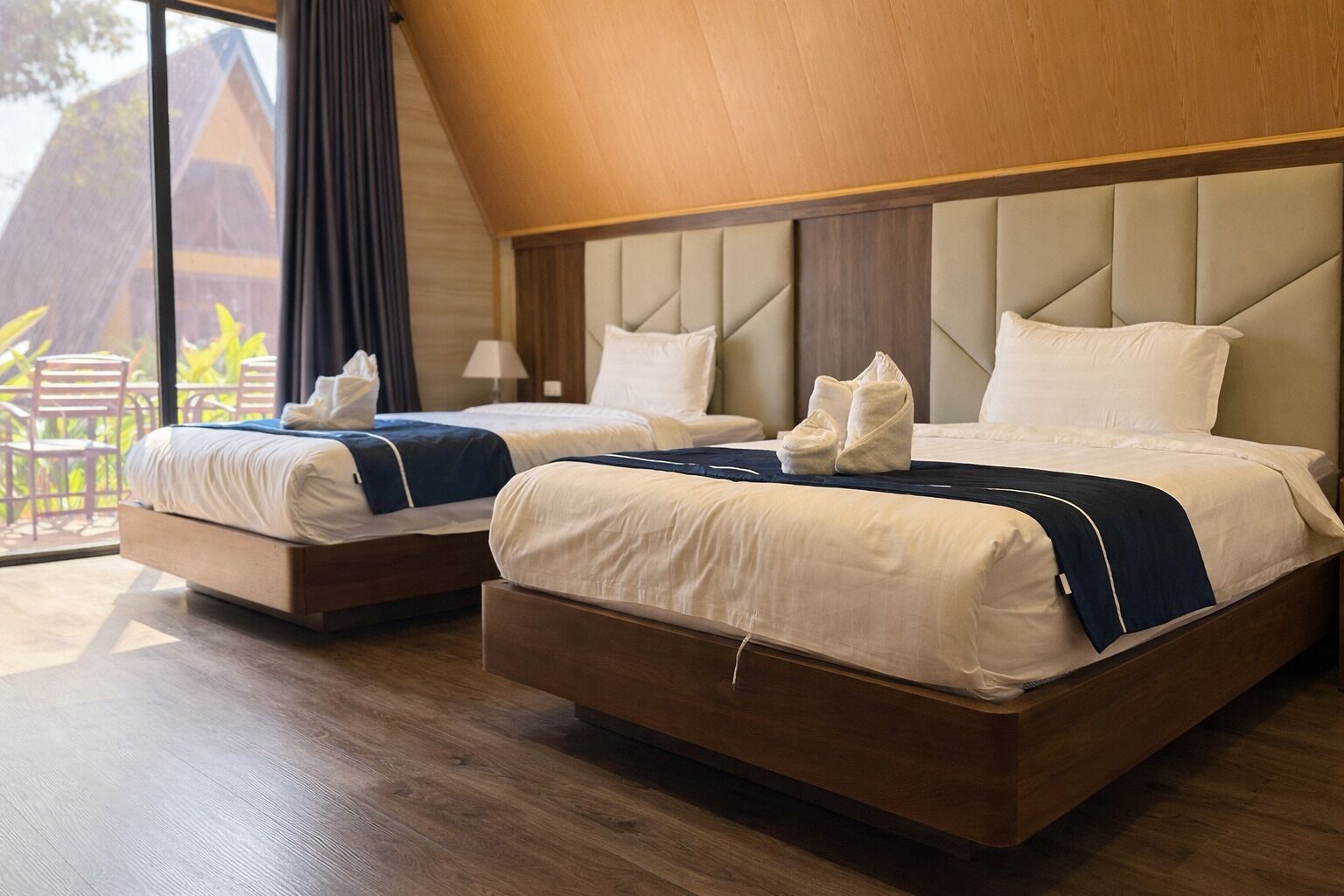 A hotel room with two beds, a wooden floor, and a view of the outdoors.