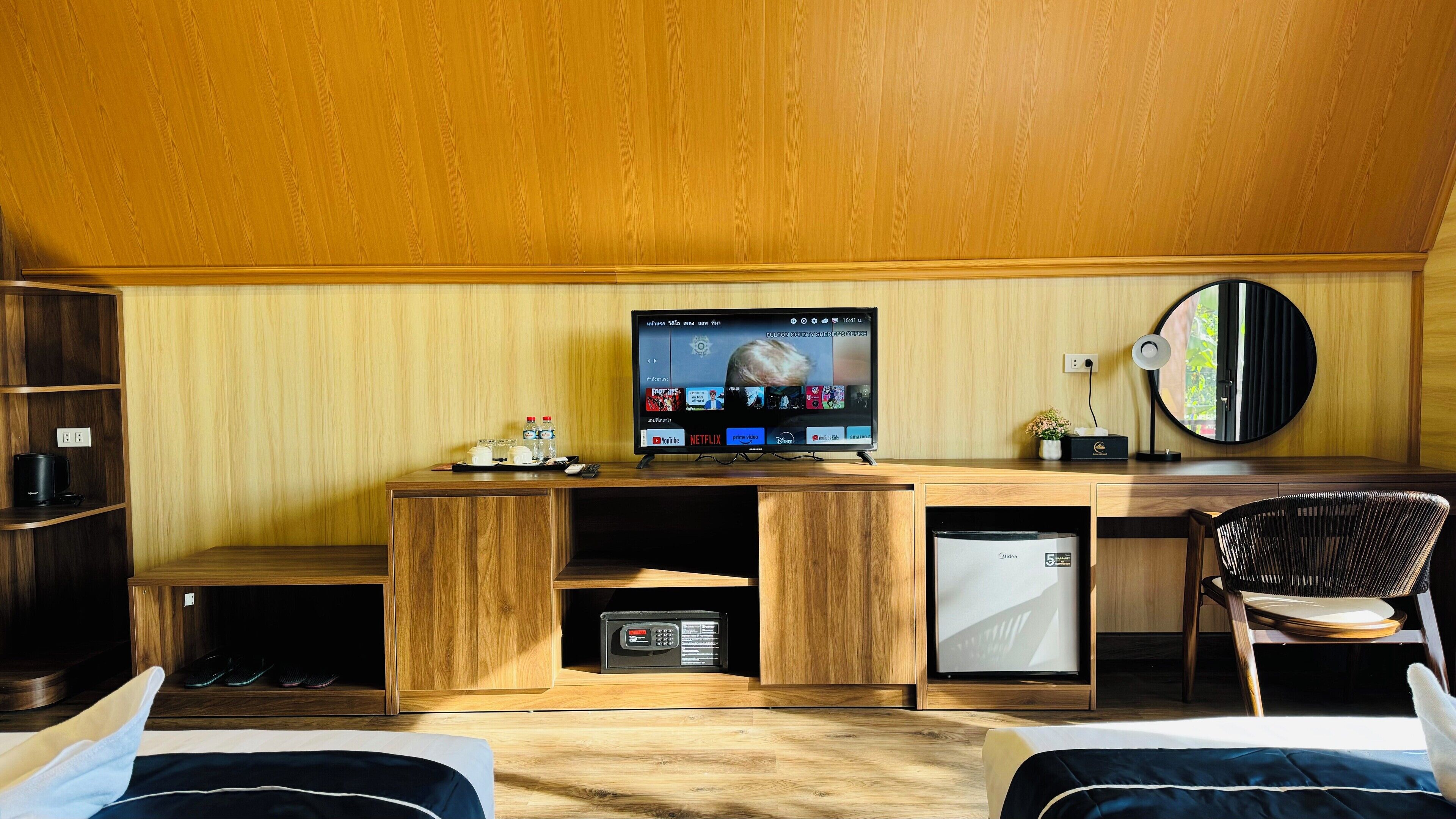 Ein kleines Zimmer mit einem Holztisch, einem Fernseher, einer kleinen Kühlschrank, einem Sessel und einem Bett.