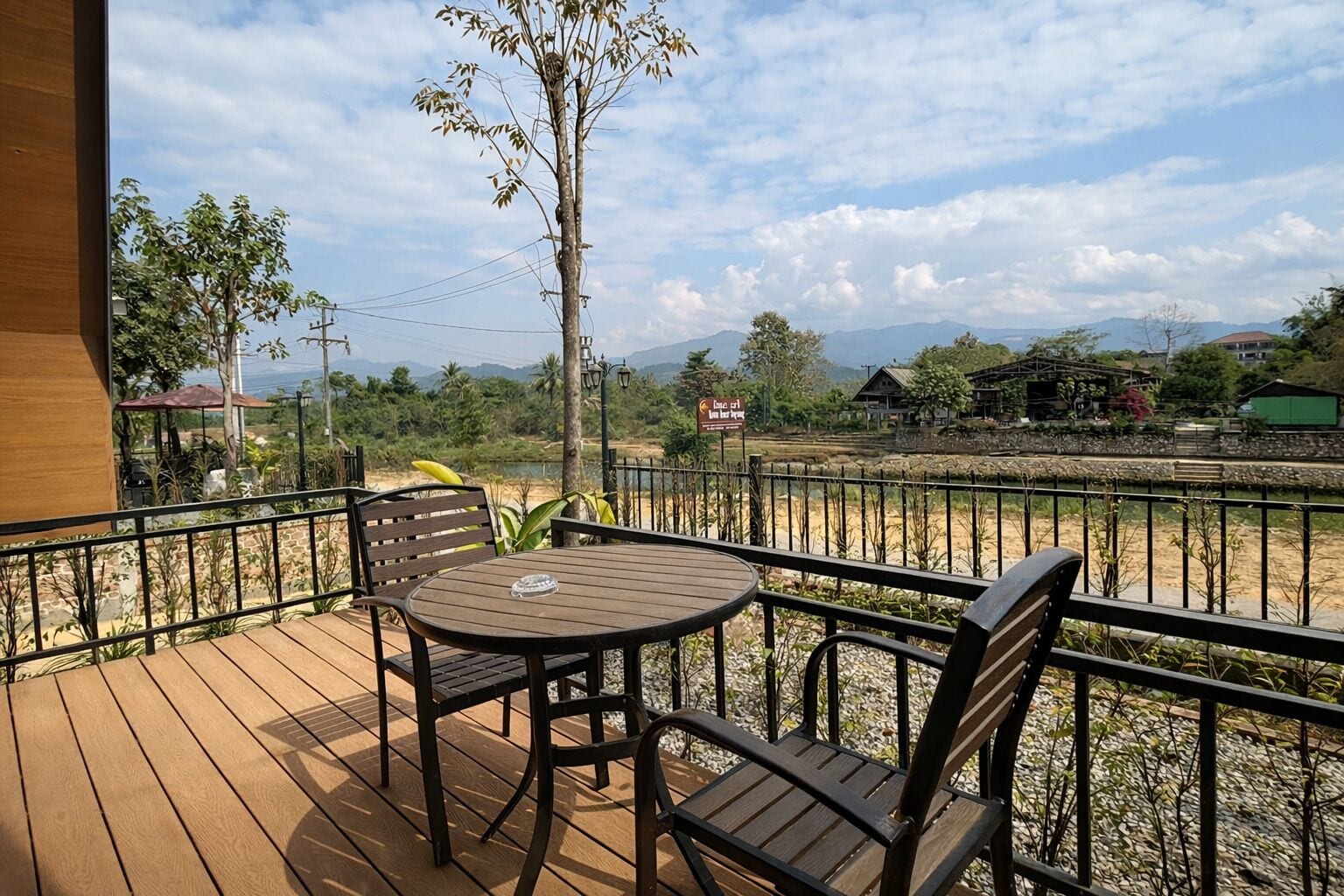 A wooden deck with a table and chairs, overlooking a beach and mountains.