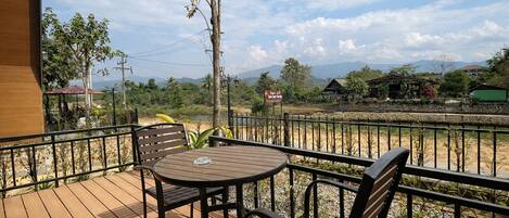 A wooden deck with a table and chairs, overlooking a beach and mountains.