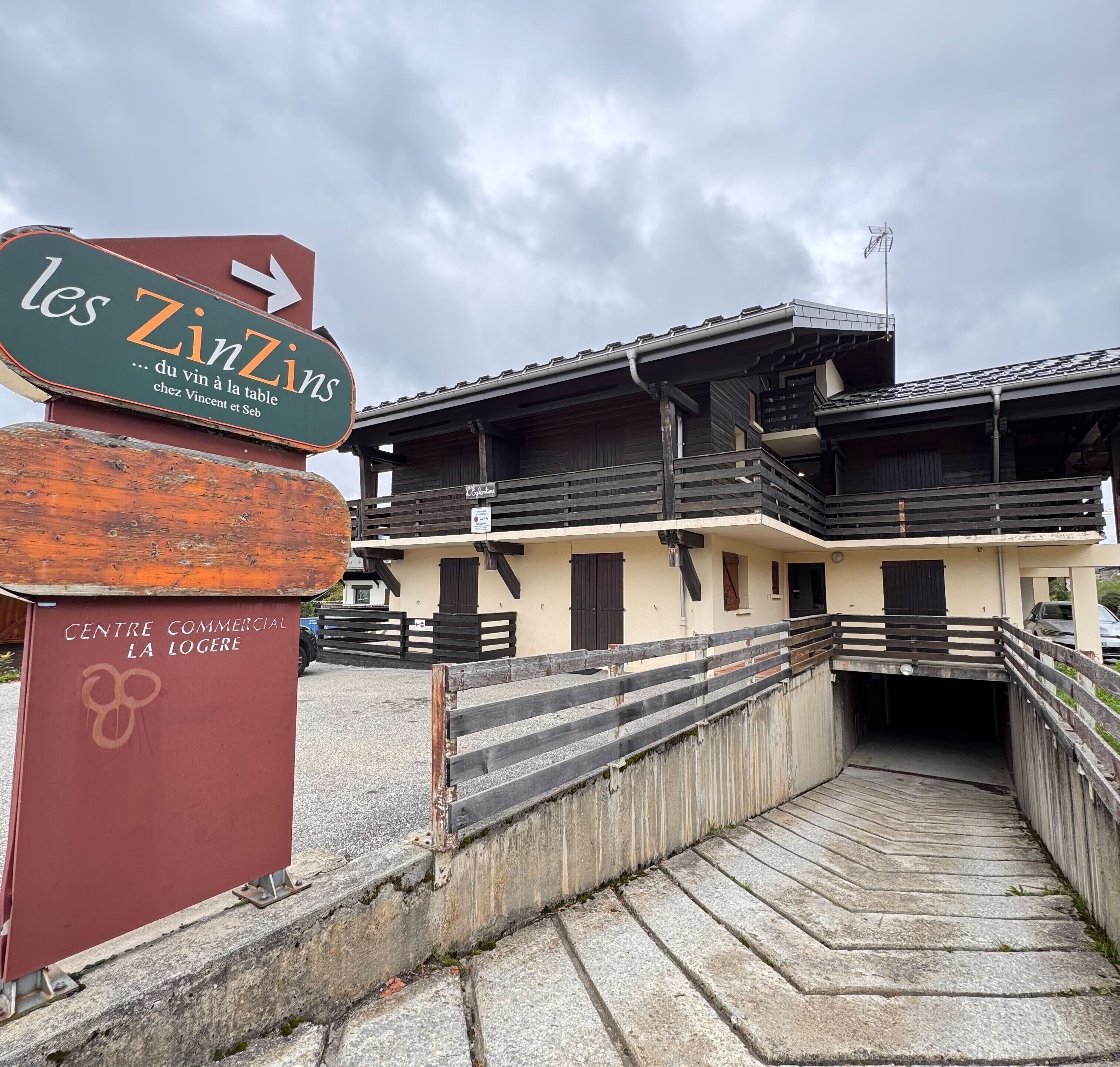 A building with a sign for 'les Zins' and a wooden staircase leading to a covered entrance.