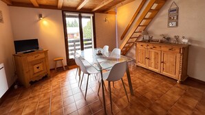 A dining area with a wooden ceiling, a glass table with chairs, a wooden cabinet, and a TV on a wooden cabinet. - Alpine stay at the foot of the slopes (Crest-Voland)