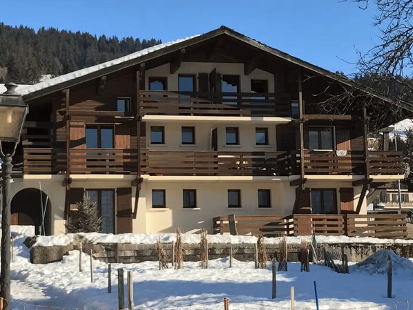 A multi-story wooden building with balconies, a snow-covered ground, and a mountainous backdrop.