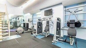 A modern gym with cardio machines, weightlifting equipment, and a large mirror. - Stylish 2BR at the Historic Mansfield Residence (New York)