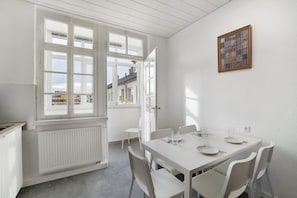 A dining area with a white table and chairs, a window with a view, and a framed picture on the wall.