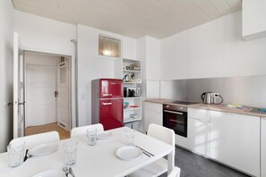 Una cocina moderna con armarios blancos, un refrigerador rojo y una mesa de comedor con platos y vasos.