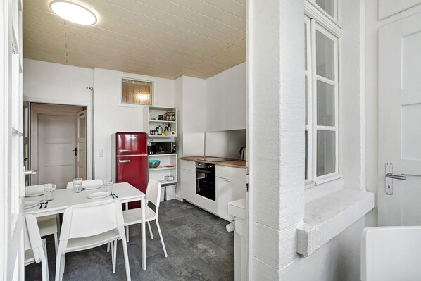 Cocina compacta con muebles blancos, un refrigerador rojo y un comedor con sillas blancas.
