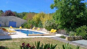 Ein Swimmingpool mit gelben Liegestühlen, umgeben von Grünpflanzen und einer blauen Wand.