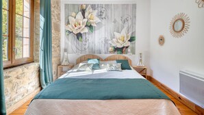 Ein Schlafzimmer mit einem großen Bett, einer Steinwand, einem Fenster mit Vorhängen und einem an der Wand befestigten Kunstwerk.