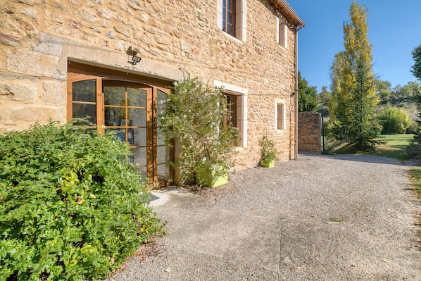 A stone building with a gravel driveway, a wooden door, and a small garden area.