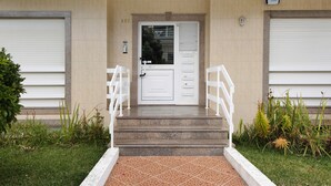 A building entrance with a white door, steps, and a small garden area with plants. - Barra Sol - Farol na Praia Apartment with Shared Pool, Balcony, and Wi-Fi (Praia da Barra)