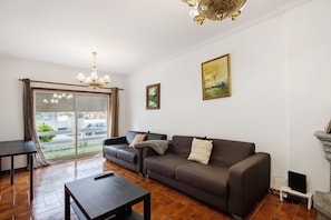 A living room with a sofa, a table, a chandelier, and a painting on the wall. - Apartment 'Barra Sol - Lighthouse On The Beach' with Shared Pool, Balcony and Wi-Fi (Praia da Barra)