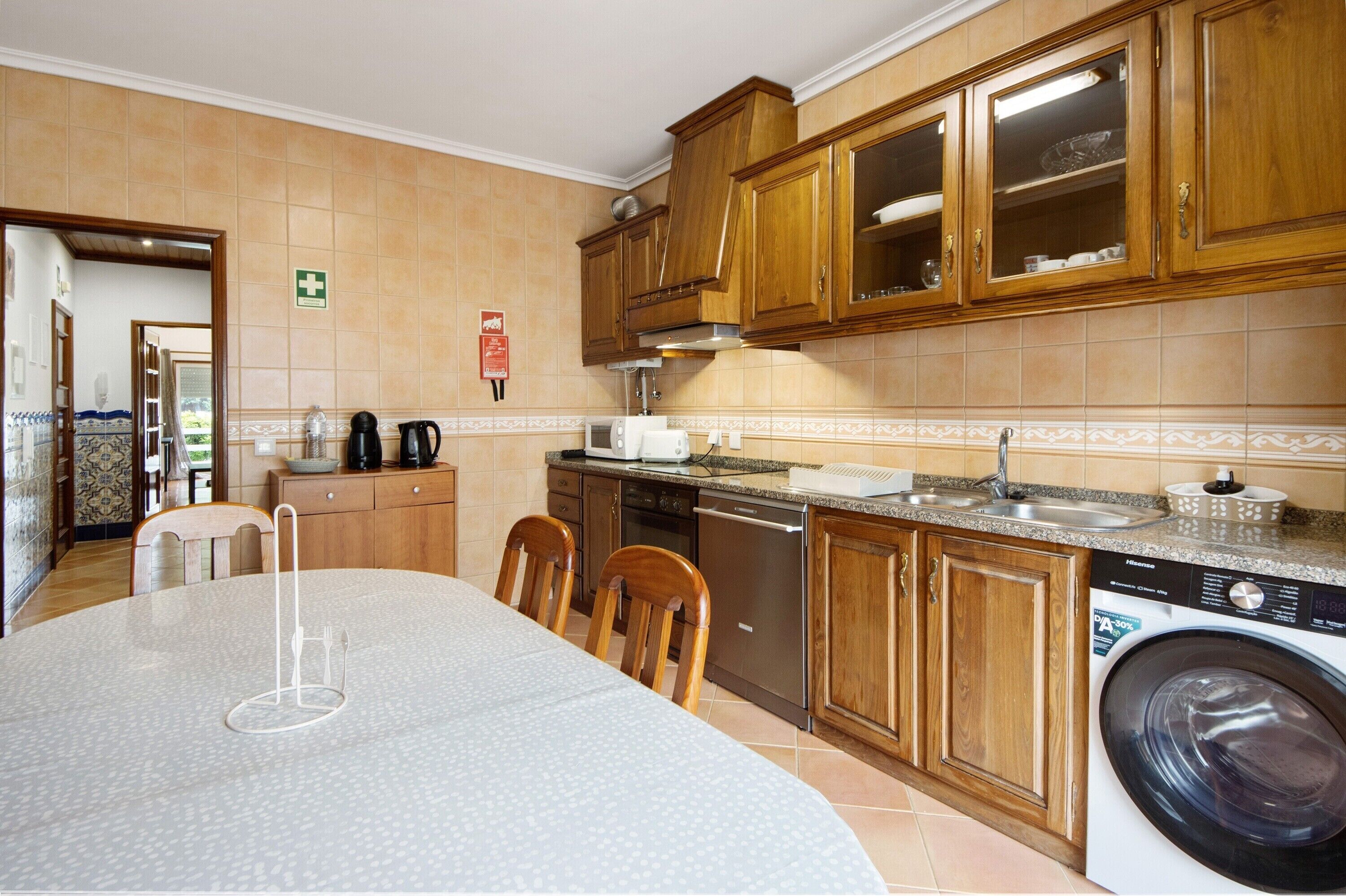 Cocina con armarios de madera, lavadora, pileta y comedor con sillas.