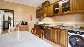 Cocina con armarios de madera, lavadora, pileta y comedor con sillas.