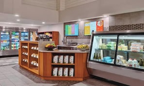 A self-service food area with refrigerated beverage dispensers, a fruit display, and a refrigerated section with packaged goods.