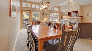 Un comedor espacioso con una mesa y sillas de madera, una chimenea de piedra y ventanas amplias que dejan entrar luz natural.