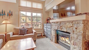 Una sala de estar con chimenea de piedra, un sofá, una mesa de centro y vistas al exterior a través de grandes ventanales.