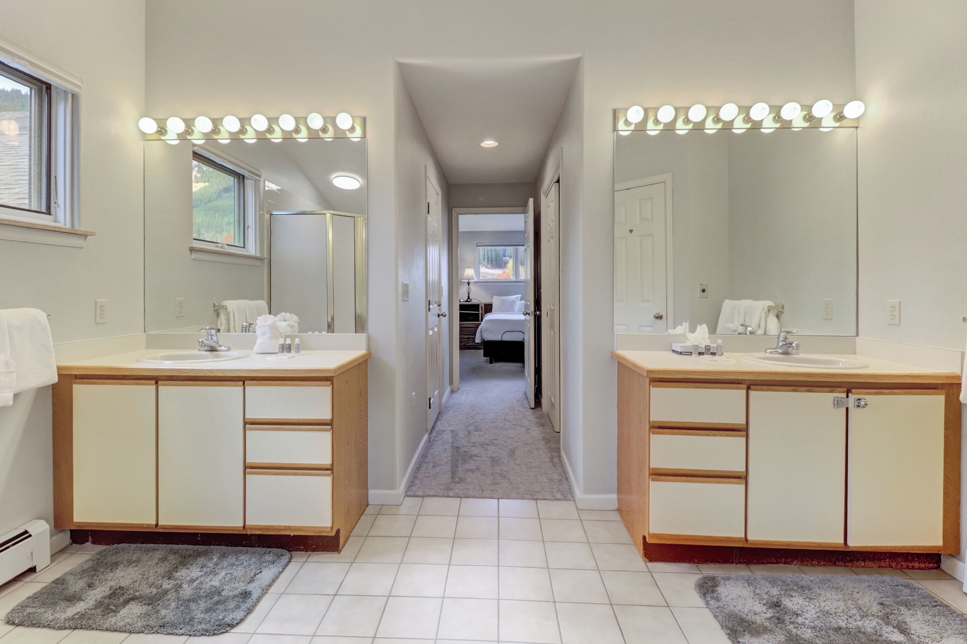 Une salle de bain d’hôtel avec deux lavabos, de grands miroirs et un couloir menant à une chambre.