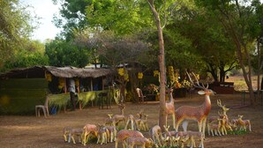 Un conjunto de estatuas de ciervos en un entorno natural, con árboles y una cabaña rústica al fondo.