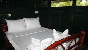 Una cama con ropa de cama y almohadas blancas, un cabecero de madera y una ventana con vista a árboles.