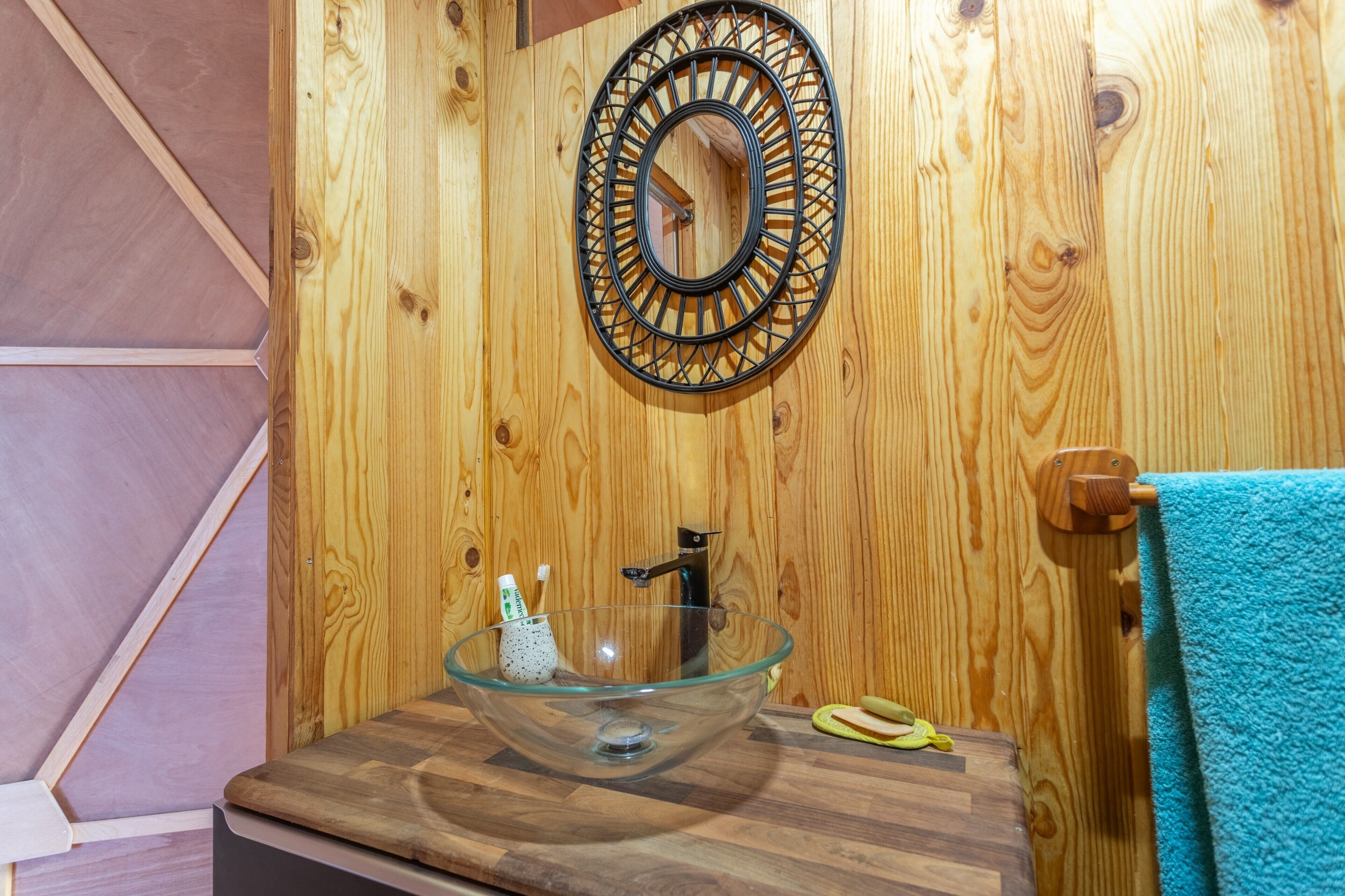 Un interior de madera con un lavabo de cristal, un toallero de madera y un espejo circular en la pared.