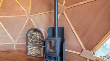 Un poêle à bois installé dans une structure ressemblant à une tente, dotée d’un plafond en bois hexagonal et d’une fenêtre.
