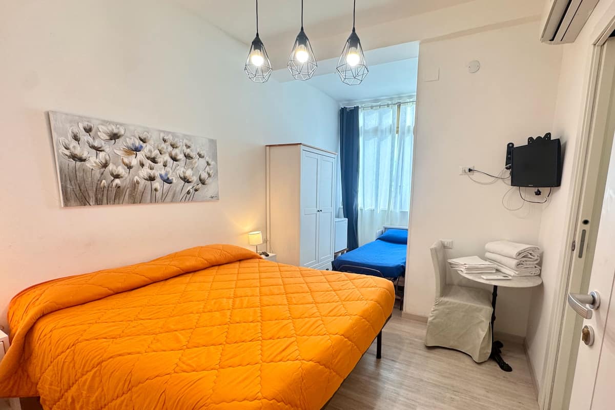 Et hotelværelse med en stor orange seng, et blomsterbillede på væggen, et lille rundt bord med håndklæder og et garderobeskab.