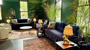 Uma sala de estar com parede verde, sofá azul, poltrona branca, mesa de centro e tapete estampado.