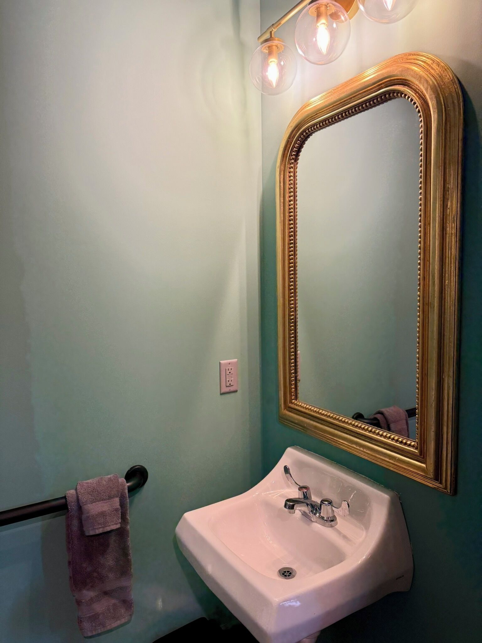 A bathroom with a white sink, a gold-framed mirror, and a towel hanging on a rack.